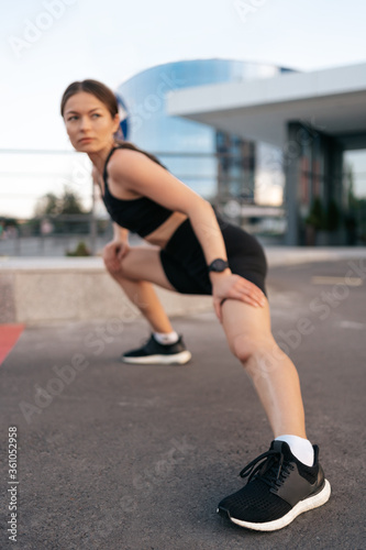 Athlete woman preparing for running on the city street. Legs warming and stretching. Sport tight clothes. Horizontal. 30s