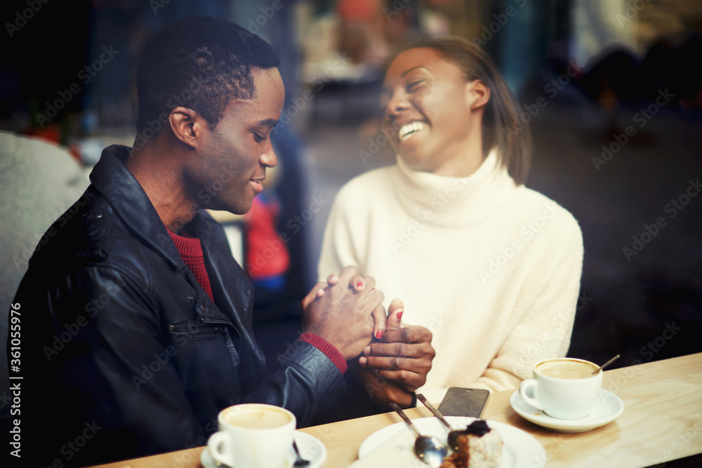 Happy black man and woman having fun time together while get warm in restaurant after strolling in cold winter day, cheerful woman sitting with her boyfriend in modern cafe bar during coffee break