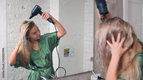 Pretty young woman drying hair with dryer in bathroom