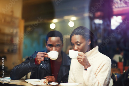 Black man and woman best friends drinking hot cappuccino while get warm together after walking outdoors in cold winter day  two dark skinned people relaxing in coffee shop during morning breakfast