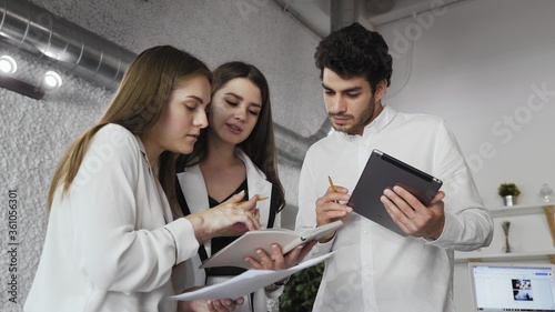 Three young corporate executives standing in lobby of modern building discussing business using digital tablet and notebook