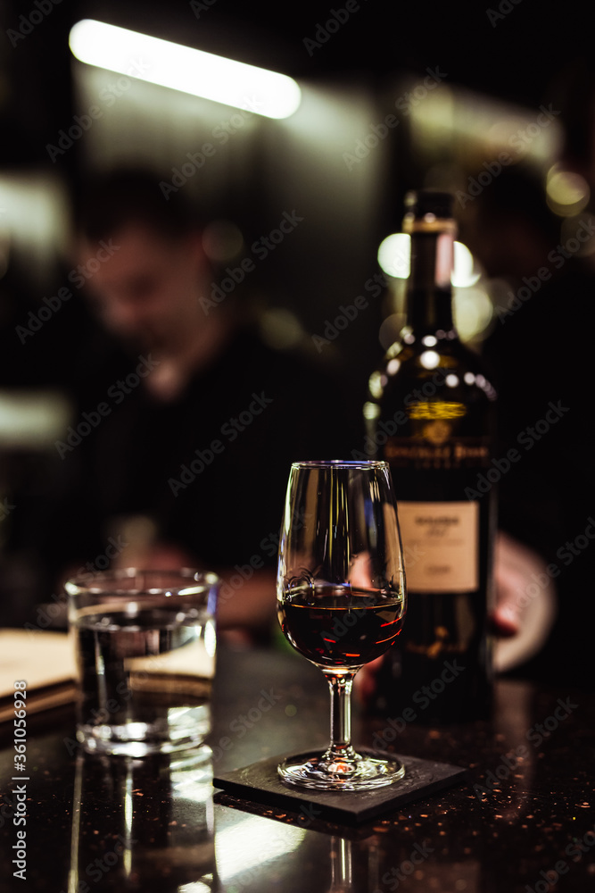 A glass and a bottle of sherry, a glass of water in a dark and moody bar atmosphere, selective focus