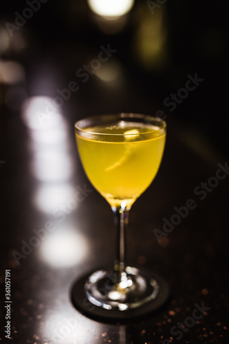 A sour cocktail in a nick and nora glass in a dark and moody atmosphere of a bar