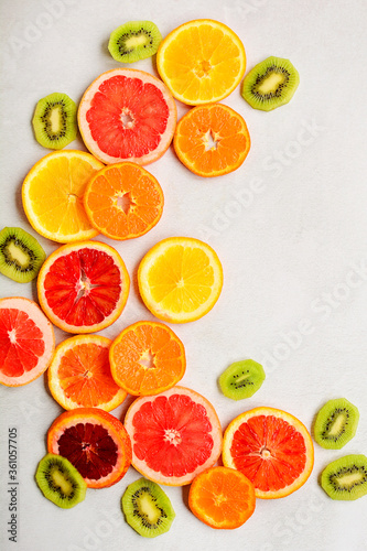 Vertical layout of circles of red orange, tangerines, grapefruit and slices of kiwi on a light gray background.