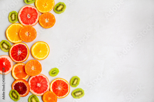 Bright layout of slices of kiwi  slices of red orange  tangerines  grapefruit on a light gray background. Side space for design.