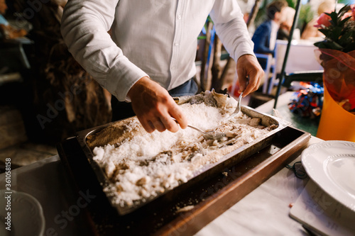 The chef chops the fish baked in salt.