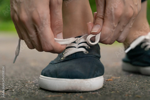 Close-up of women s hands tying shoelaces in dark blue sneakers on a jog in the woods.