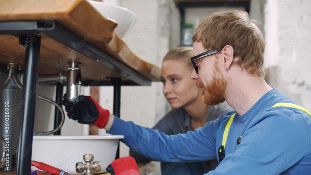 Housewife controlling plumber assembling sink pipes Housewife controlling plumber assembling sink pipes