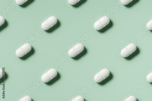 medicine, healthcare and pharmacy concept - white pills or capsules lie in rows diagonal on mint green background top view copy space pattern