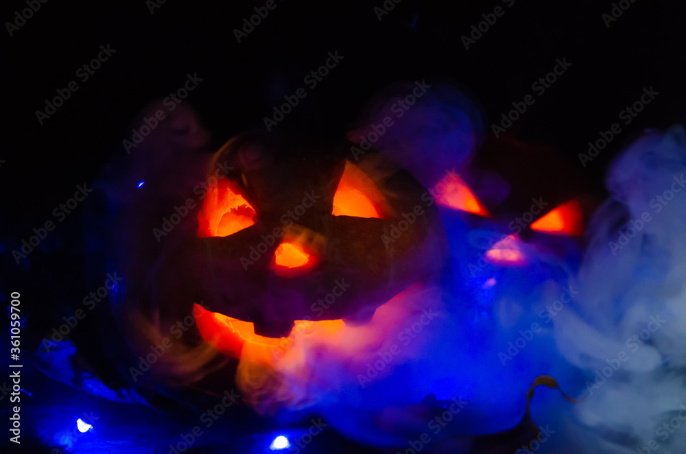 Two glowing pumpkins in the dark in the smoke in the forest close-up. One pumpkin peeks out from behind another. Beautiful background for Halloween. Two glowing pumpkins in the dark in the smoke in the forest close-up. One pumpkin peeks out from behind another. Beautiful background for Halloween.