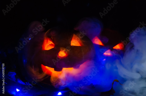 Two glowing pumpkins in the dark in the smoke in the forest close-up. One pumpkin peeks out from behind another. Beautiful background for Halloween.