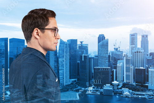 Young handsome businessman in suit and glasses dreaming about new career opportunities after MBA graduation. Singapore on background. Double exposure.