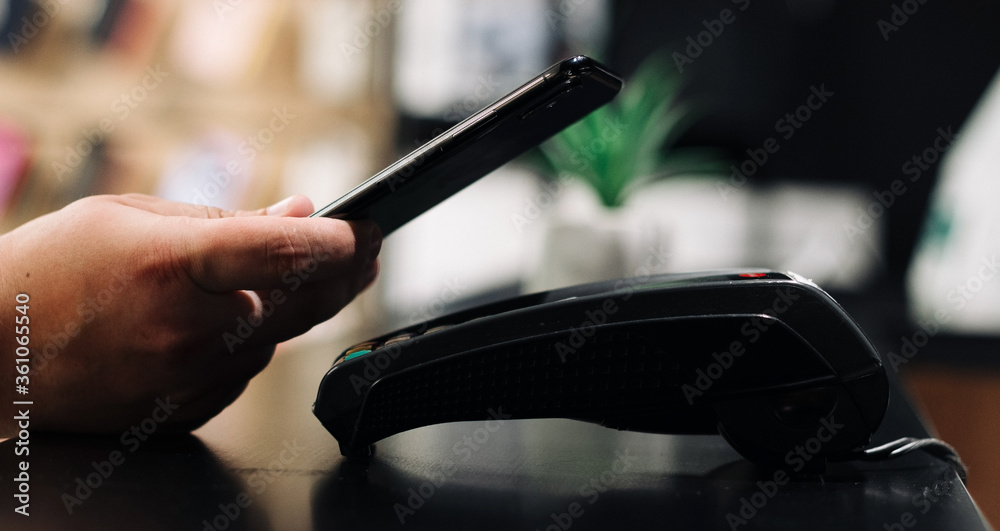 Costumer pays phone nfc terminal in the shop. Close up. Men take phone in the hand and pays in terminal. Costumer pays phone nfc terminal in the shop. Close up. Men take phone in the hand and pays in terminal.