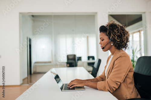 Side view portrait of a beautiful young businesswoman working with laptop and headset. © bnenin