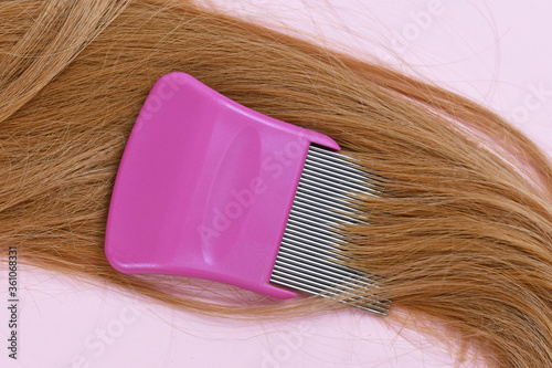 Strand of blond hair with lice comb on light pink background photo