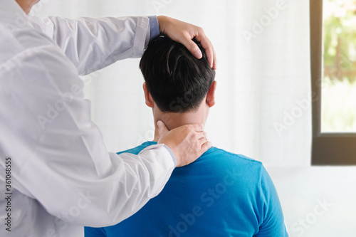 Doctor physiotherapist doing neck adjustment. stretching the Injured Neck of a Male Patient in medical office.