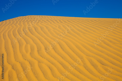 Isolated Sand dune in the desert. View on the sandy slope from the top of the sand dune. Sand texture. Sand pattern full frame photography. Sand dune surface in sunny day. Sand ripples close-up. 