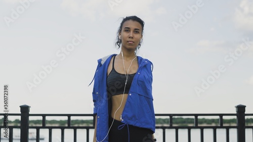 Young Afro-american woman in headphones performs stretching and warming before running © stanis88
