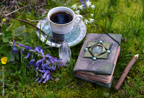 Hand crafted diary book with flowers, crystal and tea cup in the garden. Esoteric, gothic and occult background with magic objects, mystic and fairy tale concept outdoors.