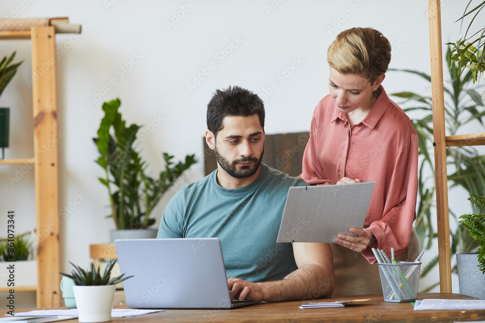 Portrait of female assistant showing documents to handsome bearded man working at desk in modern office interior Portrait of female assistant showing documents to handsome bearded man working at desk in modern office interior