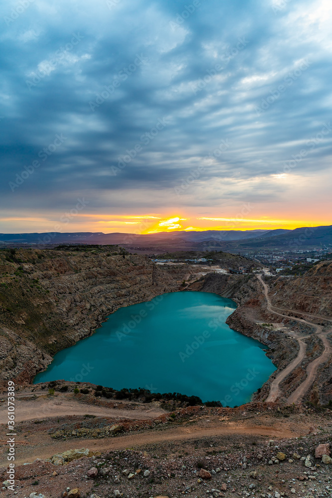 Fototapeta premium Sunrise over the blue quarry lake in the shape of a heart. Limestone fluxing of Kadykovo quarry, Balaklava, Crimea. A place for a photo shoot, tourism, beautiful places.