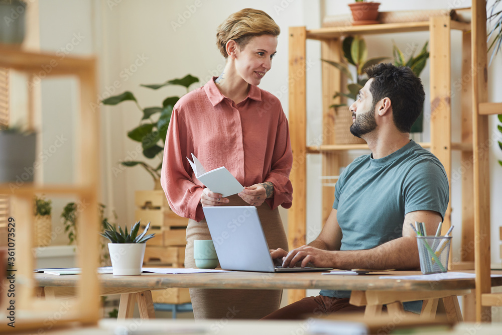 Portrait of female manager talking to handsome bearded man working at desk in modern office interior with wooden details Portrait of female manager talking to handsome bearded man working at desk in modern office interior with wooden details