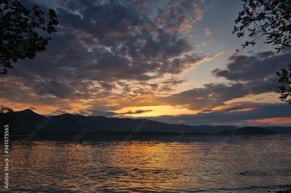 黄昏時の空と湖の風景。雲の漂う夕暮れの空と夕陽に煌めく湖面。屈斜路湖、北海道、日本。