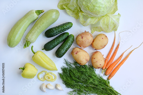 Cucumbers, cabbage, zucchini, peppers, garlic and herbs on a white background. View from above. Seasonal vegetables.