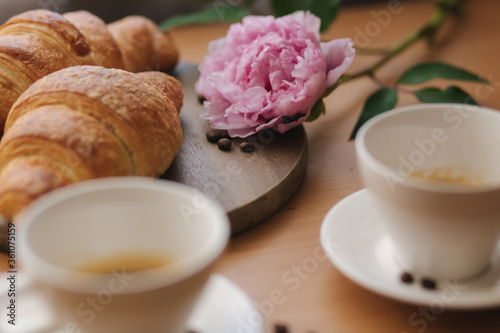 Fototapeta Naklejka Na Ścianę i Meble -  Vegan breakfast at home. Cappuccino with coconut milk and two empty vegan croissants. Morning with coffe. Pink peony flower on table