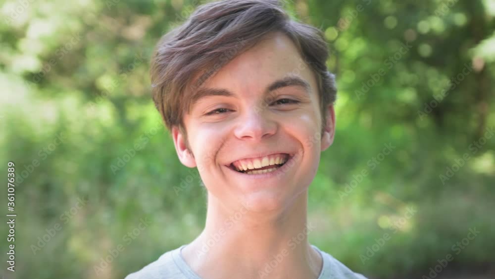Outdoors portrait of caucasian teen boy looking at camera and smiling cheerfully. Cute teenager student at green background. Handsome guy.