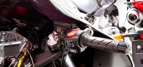 Right side of motorcycle steering wheel close-up. The handle of the gas sportbike, with windshield, mirror, control buttons for headlights, turn signals. Ignition keys in the lock. Banner for web site