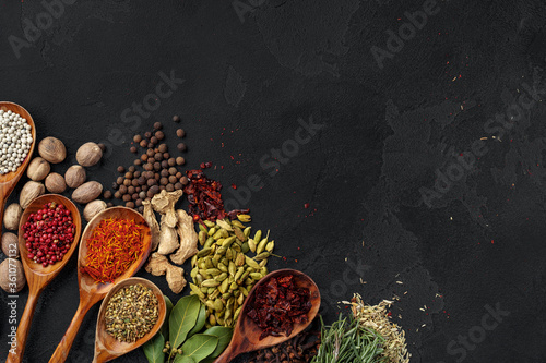 Wooden spoons with various spices on black background