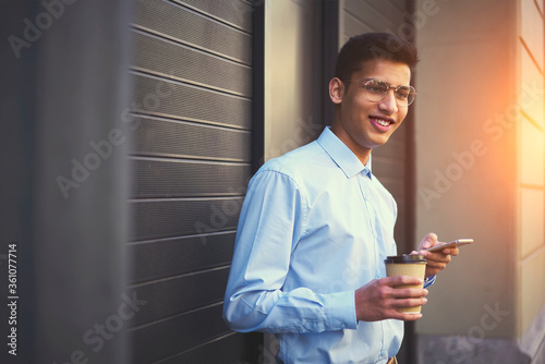 Young smiling hipster guy in good mood enjoying coffee while messaging with friends photo