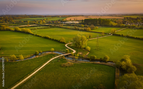 Aerial view of a winding dirt road across meadows and a bridge over the river