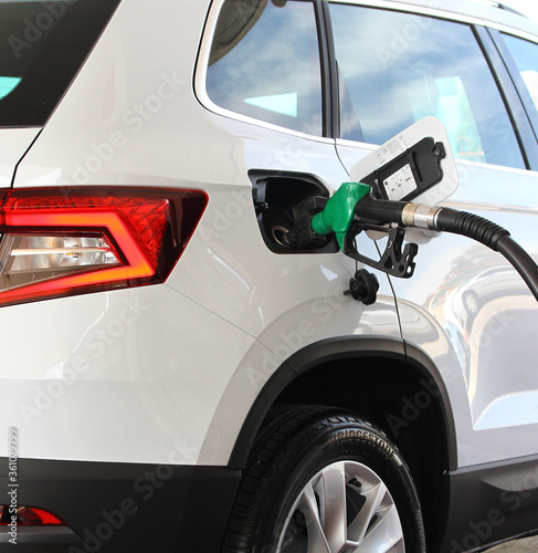 A hand holds a fuel pump and refills a car with gasoline