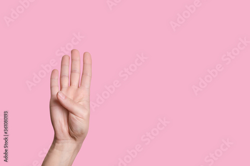 The number four. Female hand counts on fingers. pink background. © Evgenia