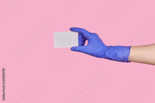 A hand in a surgical blue glove holds a blank paper isolated