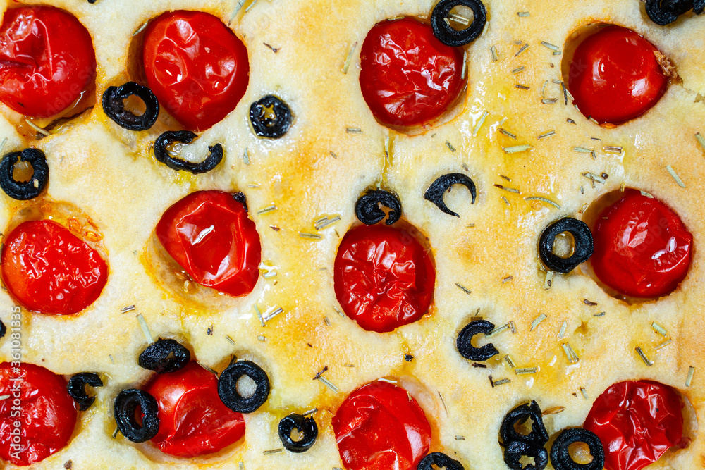 Focaccia with black olives, cherry tomatoes, rosemary and olive oil on a rustic wooden table. Focaccia with black olives, cherry tomatoes, rosemary and olive oil on a rustic wooden table.