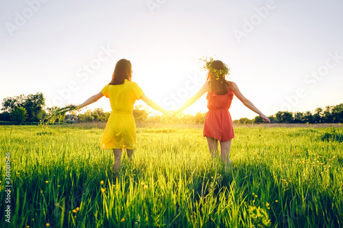 Two girls hold hands and walk in nature. Summer evening in the field