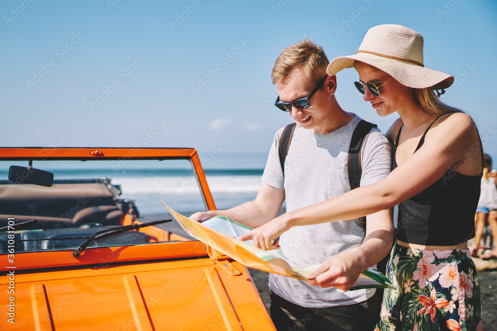 Romantic hipster couple talking about route looking at map stopping rental cabriolet for discussing destination,young guy hand girl having roadtrip resting during honeymoon on tropical island