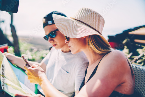 Male and female tourist reading map and using navigation app on smartphone for searching route sitting in rental car, couple of travelers browsing information on cellphone for getting to destination