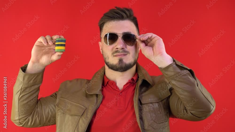 Handsome Man Holds Poker Chips Takes Off Glasses and Winks at Camera. Poker face and gambling concept. Poker Chips in Player Hand Handsome Man Holds Poker Chips Takes Off Glasses and Winks at Camera. Poker face and gambling concept. Poker Chips in Player Hand