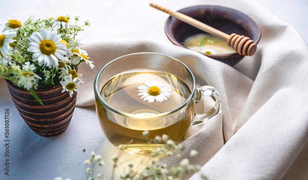 Transparent cup of hot chamomile tea and honey. Concept of a healthy soothing herbal drink after a hard day or in the morning Transparent cup of hot chamomile tea and honey. Concept of a healthy soothing herbal drink after a hard day or in the morning