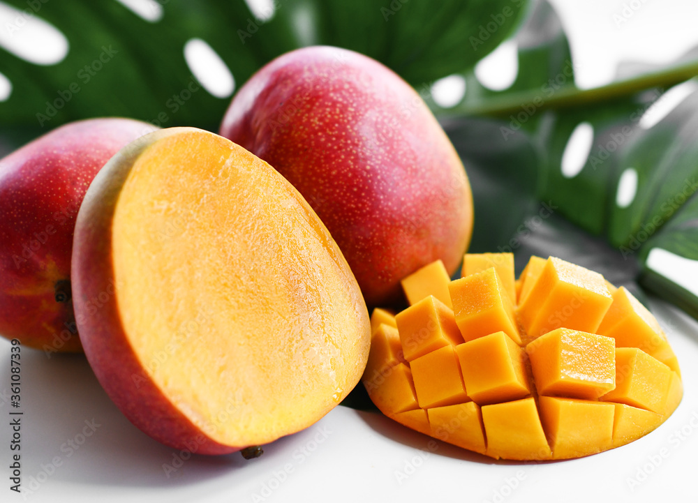 Whole, half and sliced Mango fruit on background of green tropical palm leaf. Closeup Whole, half and sliced Mango fruit on background of green tropical palm leaf. Closeup
