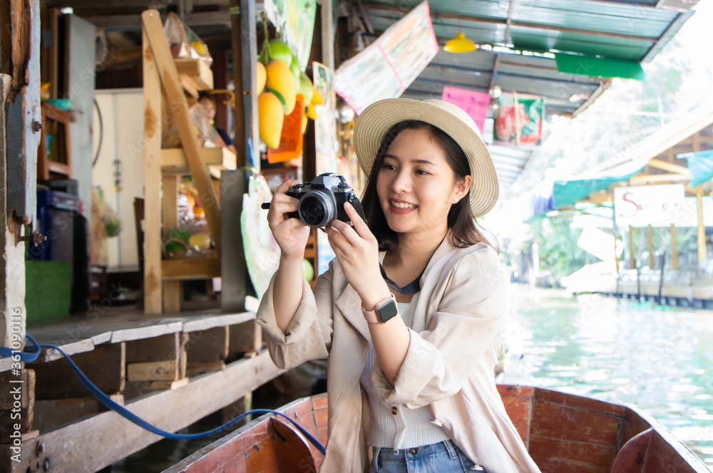 asia female tourists wearing hat holding camera and smartphone take photo vlog live. Beautiful woman take taxi boat visiting Damnoen Saduak floating market,Ratchaburi.