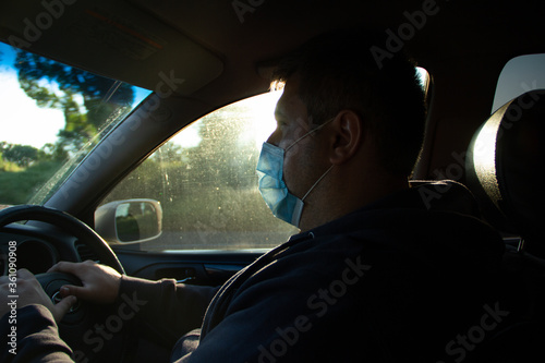 
A man in a car driving in a medical mask from a coved - 19