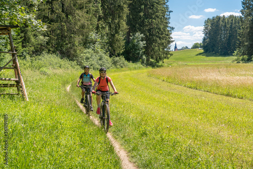 Grandmother with electric mountain bike and granddaughhter without electric help on a smooth meadow trail in the Franconian Switzerland area of Bavaria  Gemany