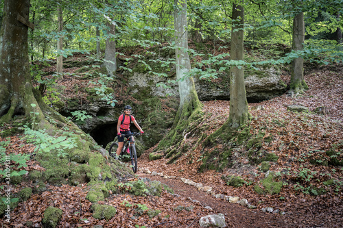 teenage girl riding her mountainbike on a forest trail in front of a cave in Franconian Switzerland, Bavaria, Germany