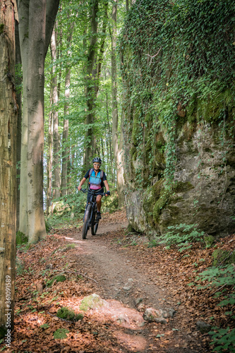 pretty senior woman underway on her electric mountain bike on a rocky forest trail in Franconian Switzerland, Bavaria, Germany