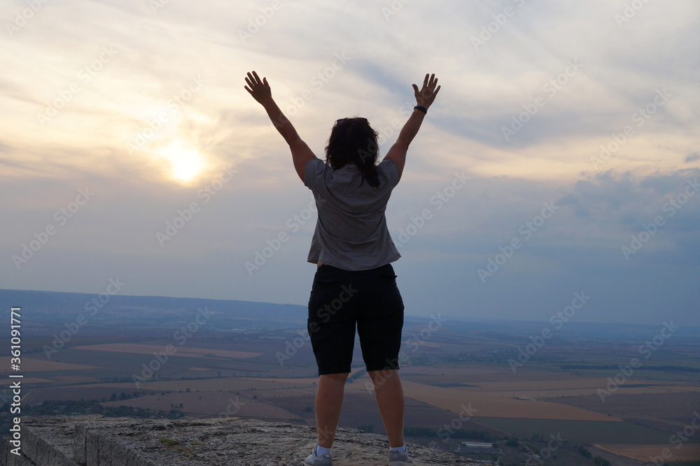 middle-aged woman of Asian appearance stands on top holding her hands up in ecstasy middle-aged woman of Asian appearance stands on top holding her hands up in ecstasy
